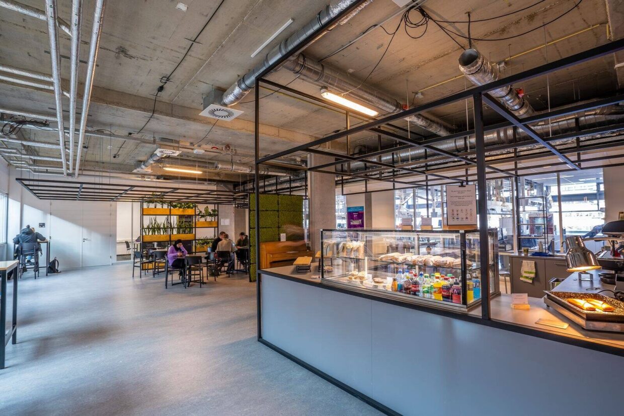 A spacious modern cafeteria with industrial design, showcasing people dining and working in a relaxed atmosphere.