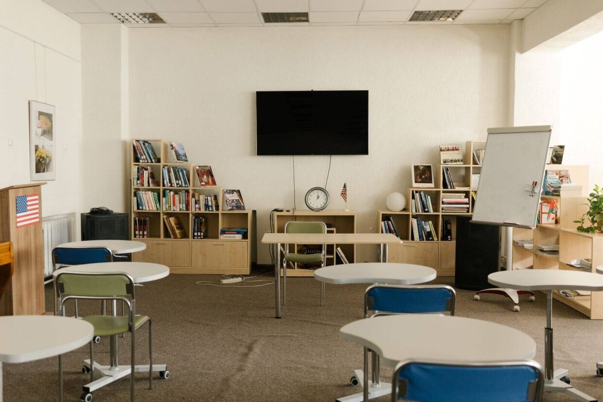 Empty classroom featuring bookshelves, whiteboard, and modern seating arrangement.