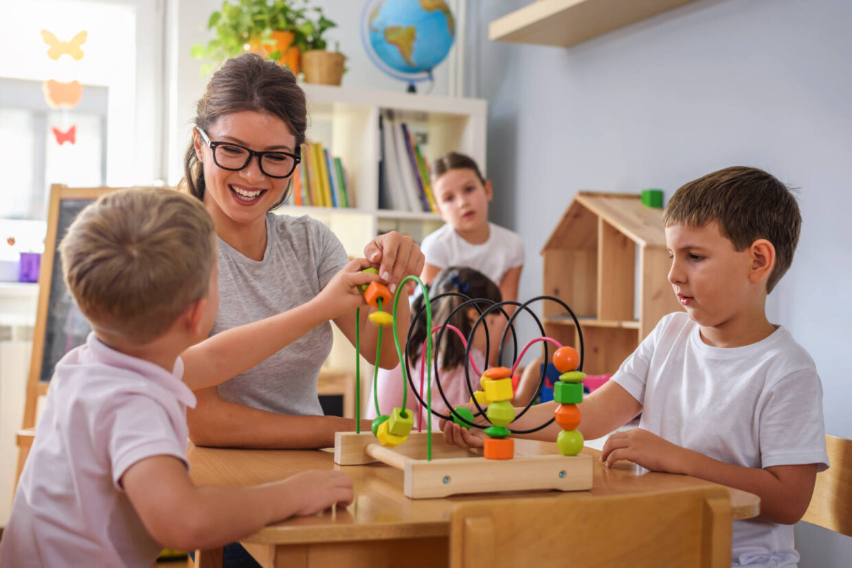 3 Kinder und eine Frau spielen an einem Holztisch